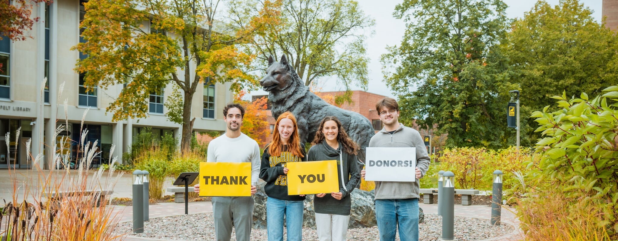 Students hold "Thank You Donors" signs in front of the Husky Statue