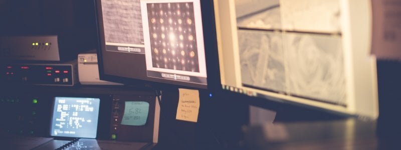 Various pieces of computer equipment in a minerals research lab. Two large computer monitors show images captured on a scanning electron microscope.