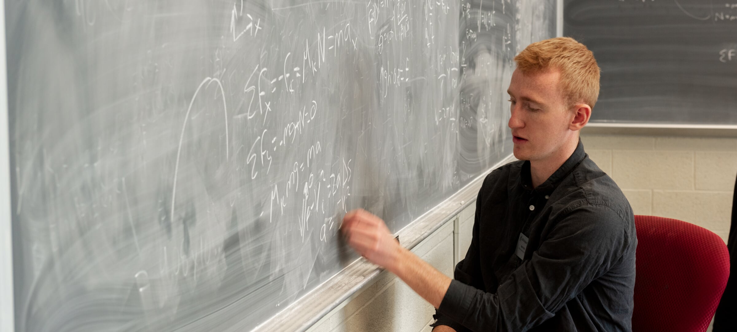 Three researchers in lab coats, gloves, and safety glasses sitting at a table with vials