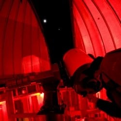 Student stands and looks through the telescope with lights dimmed.