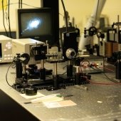 On lab table, a laser, lenses, and monitor