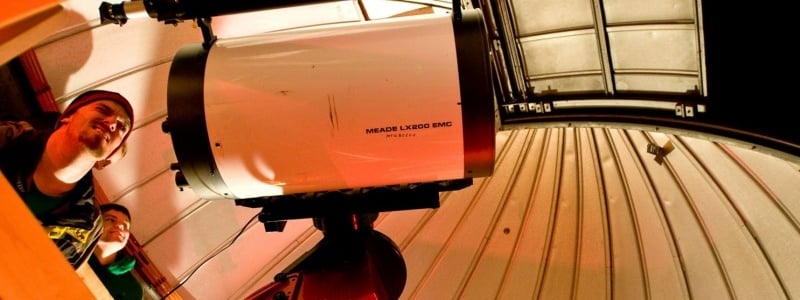 Two students looking through a large telescope inside an observatory