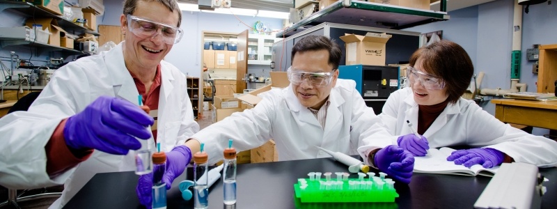 Yoke Khin Yap and two researchers at a table inspecting vials of liquid in Dr. Yap's laboratory