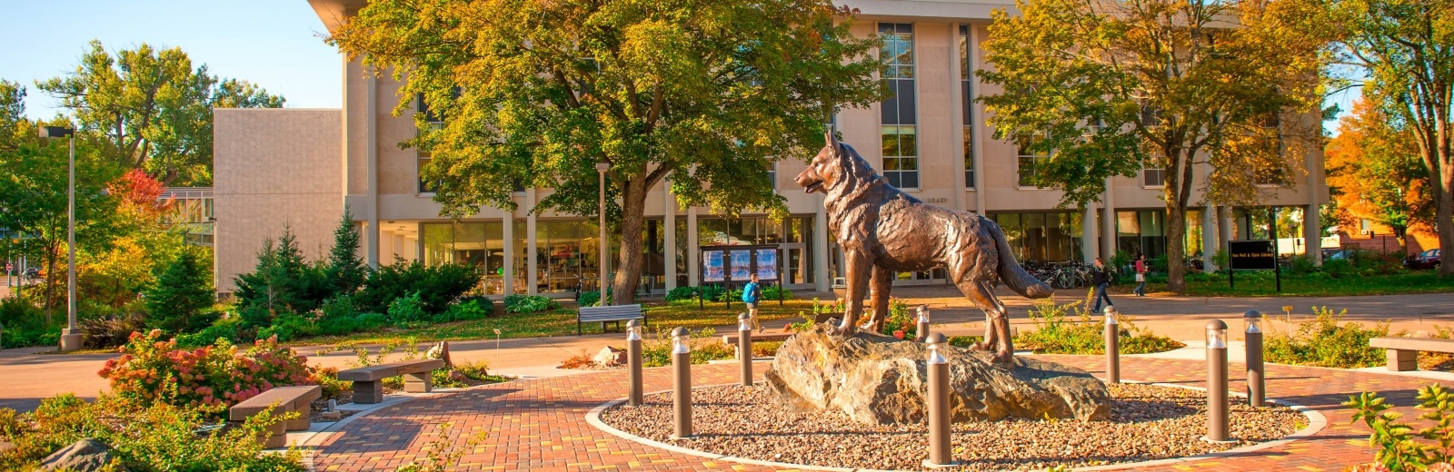 Bronze husky statue in the center of campus with the Library in the background.