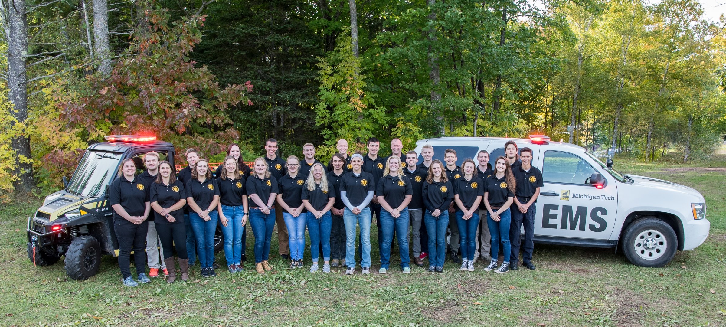 Image of 27 members of Michigan Tech's emergency medical technician team standing in front of their vehicles
