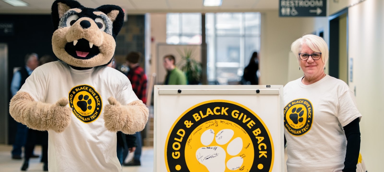 Image of Blizzard standing next to a Gold and Black Give Back sign