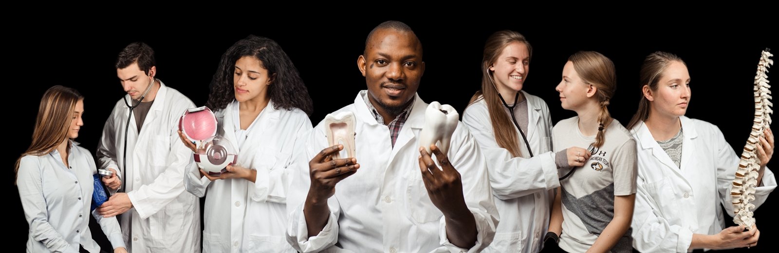 Pre-Health Professions students in lab coats holding different objects with some interacting with student patients