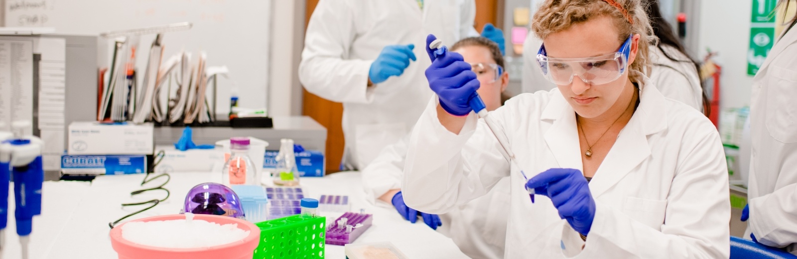 Two students and faculty inside Biological Sciences lab, student using pippette to put solution into a vial.