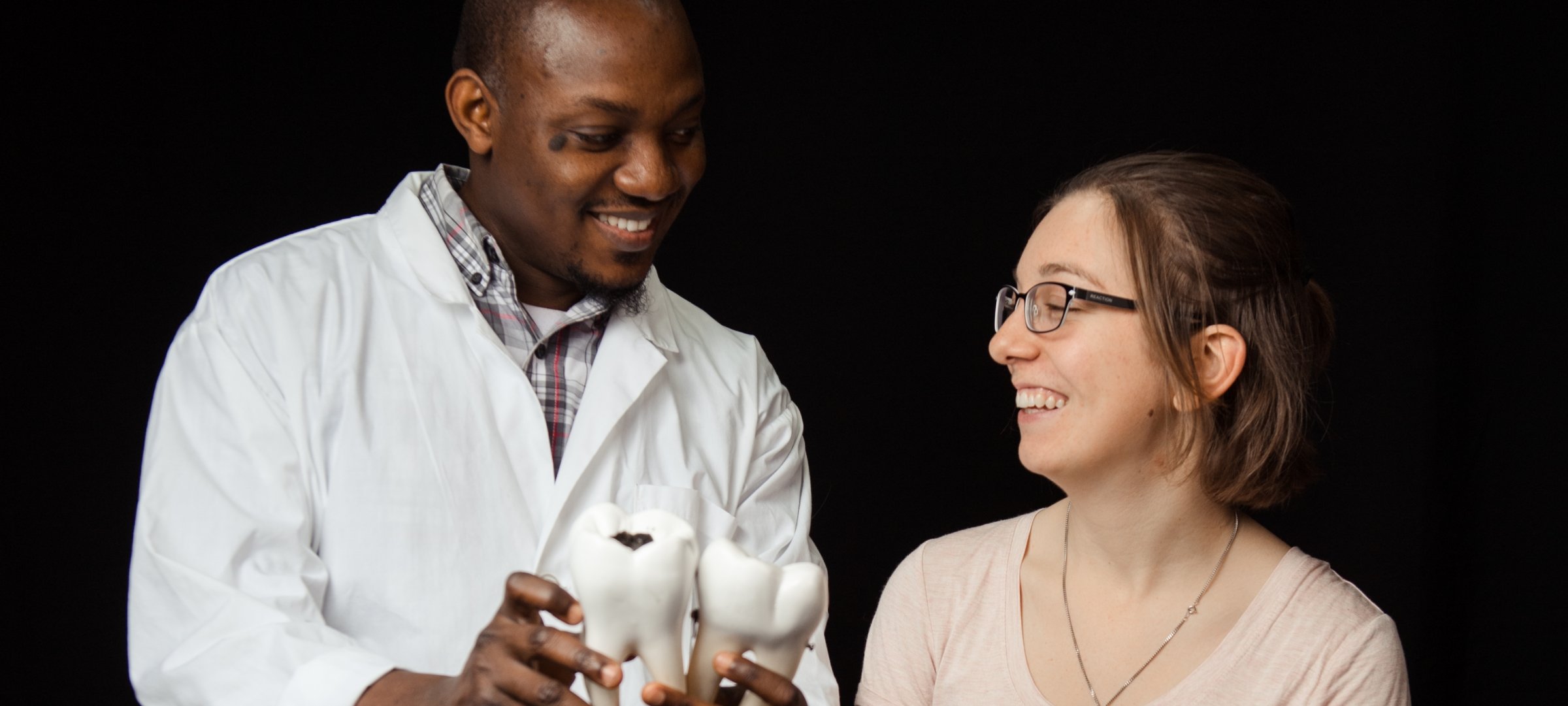 Male dentist in a lab coat showing a patient a model of a tooth.