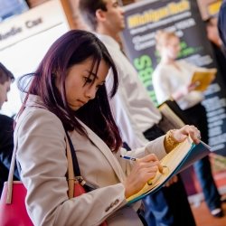 Standing student in business attire writing in a notebook