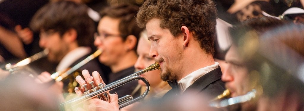 Students playing trumpets with a choir behind.