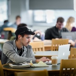 Student sitting at a round table with chairs looking at his laptop