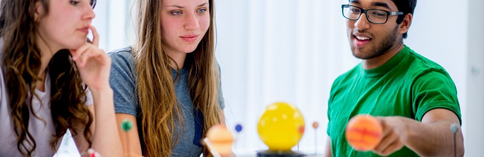 Male researcher pointing to a model of our solar system while two female students look on.