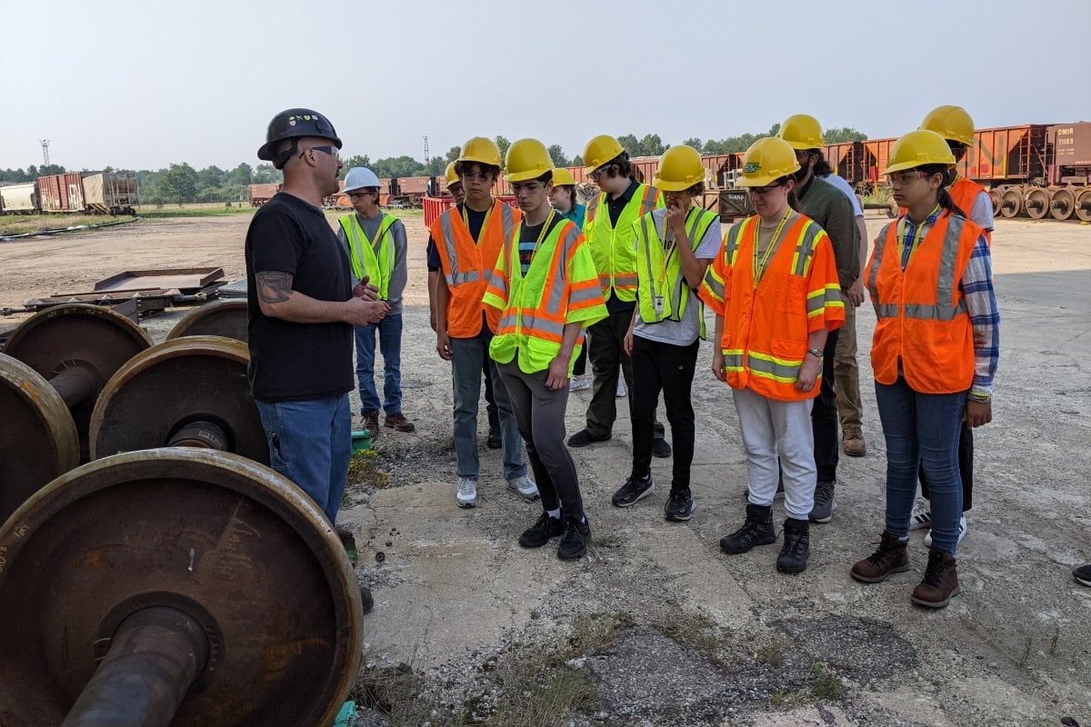 Small group of students in high visibility gear outside in a rail yard.