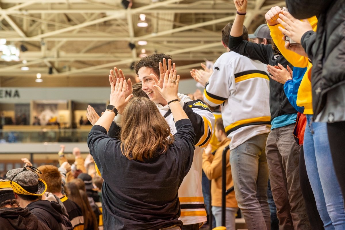 Cheer on your favorite Huskies athletic team. Students in the stands cheering at a hockey game.