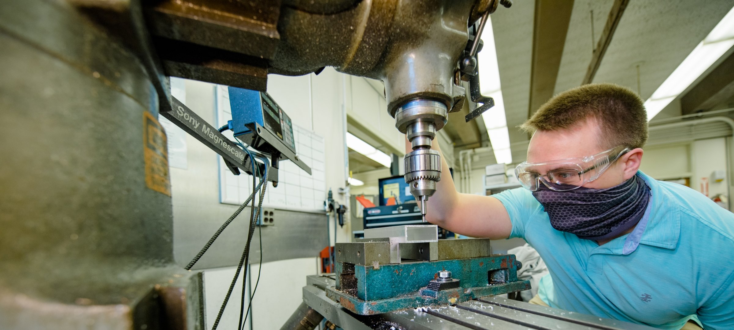 Student with protective gear using a drill press.