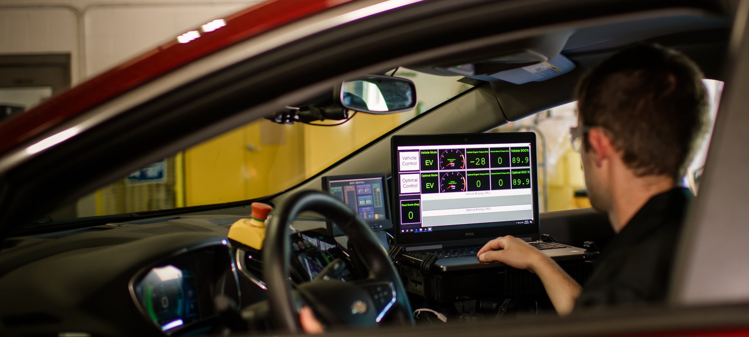 A man in the drivers seat of a car holds a laptop with a map on the screen.