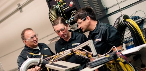 Three men in safety glasses work on a power system.