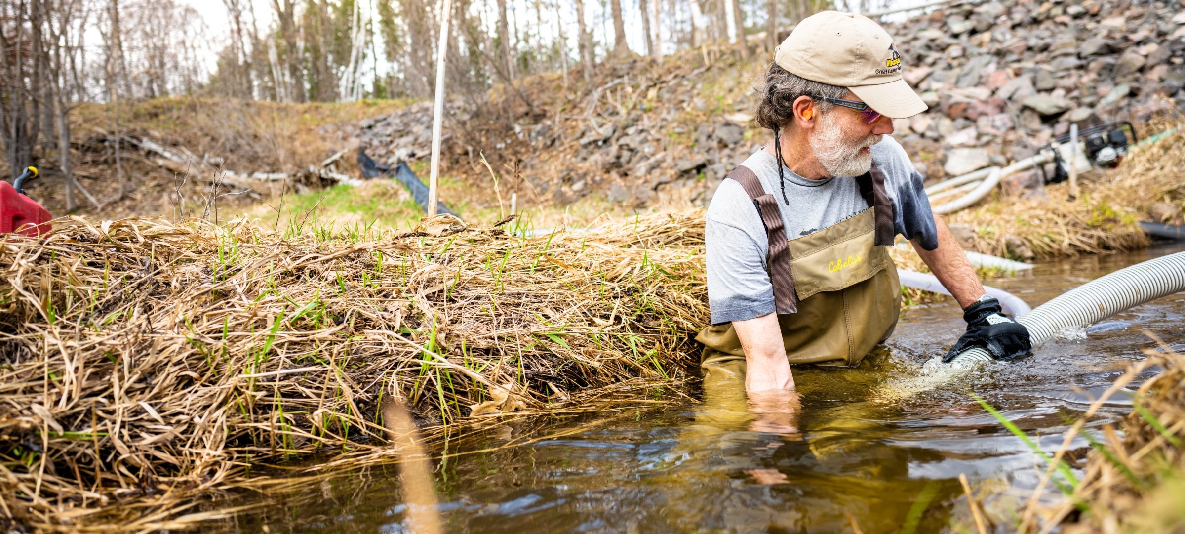 Researcher in waders in a stream holding a pipe underwater