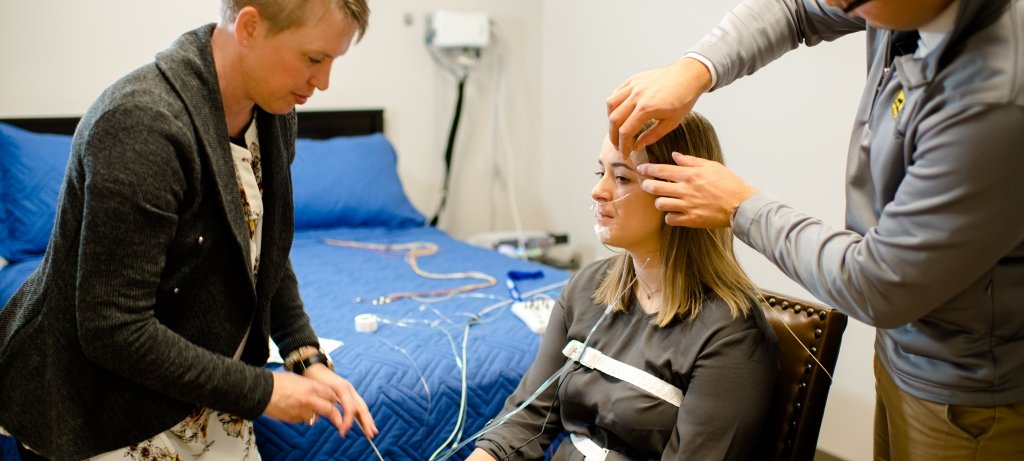 Researchers applying sleep monitoring equipment to participant