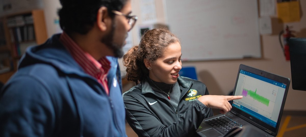 A researcher pointing to a graph on a computer screen.