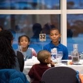 A group of children site a round table looking on.