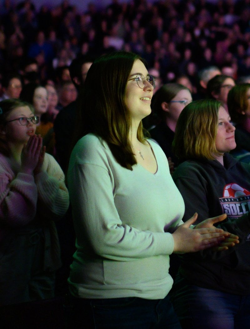 A person smiles gently while clapping in a full auditorium