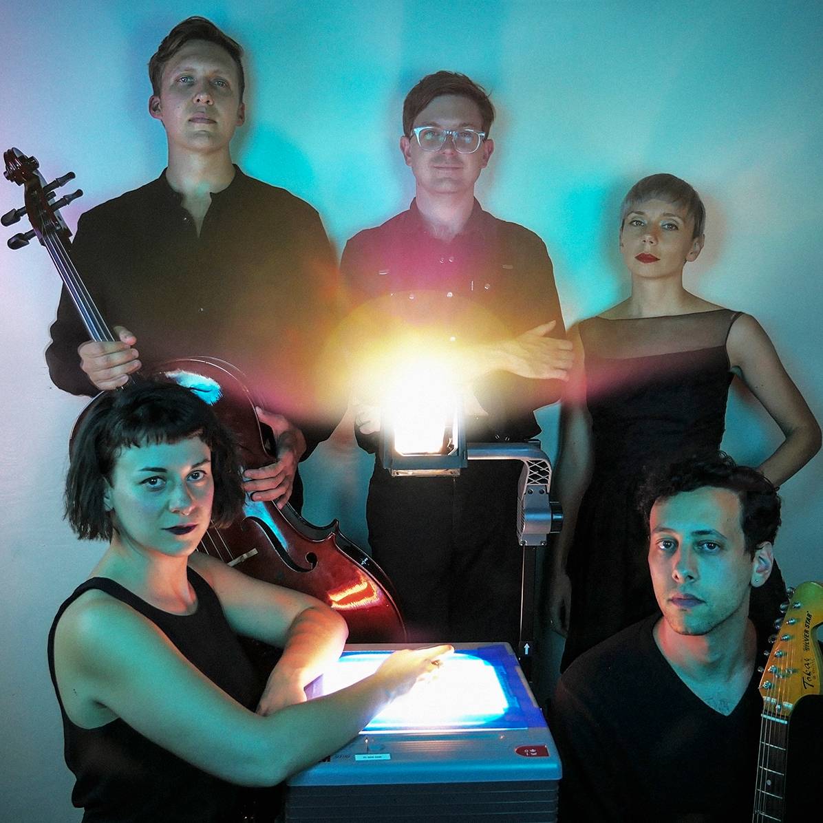 Manual Cinema group photo with five performers gathered around an overhead projector.