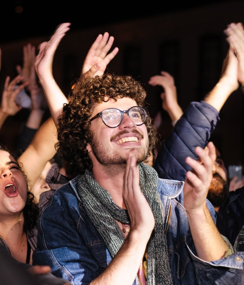 man in an audience claps while looking up at the stage