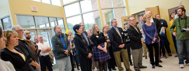 Faculty and staff standing inside the lobby of the Waatara Center watching a presentation.