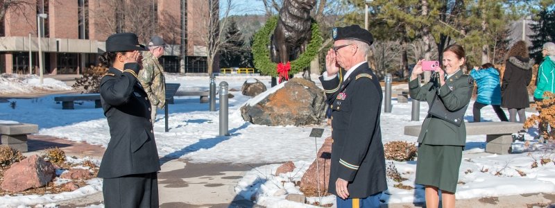 Cadet salutes a veteran in front of the Husky Statue.