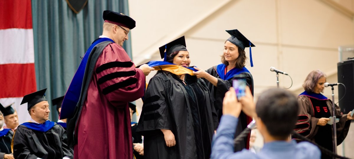 Dean Hemmer and faculty place hood on graduate student at commencement.