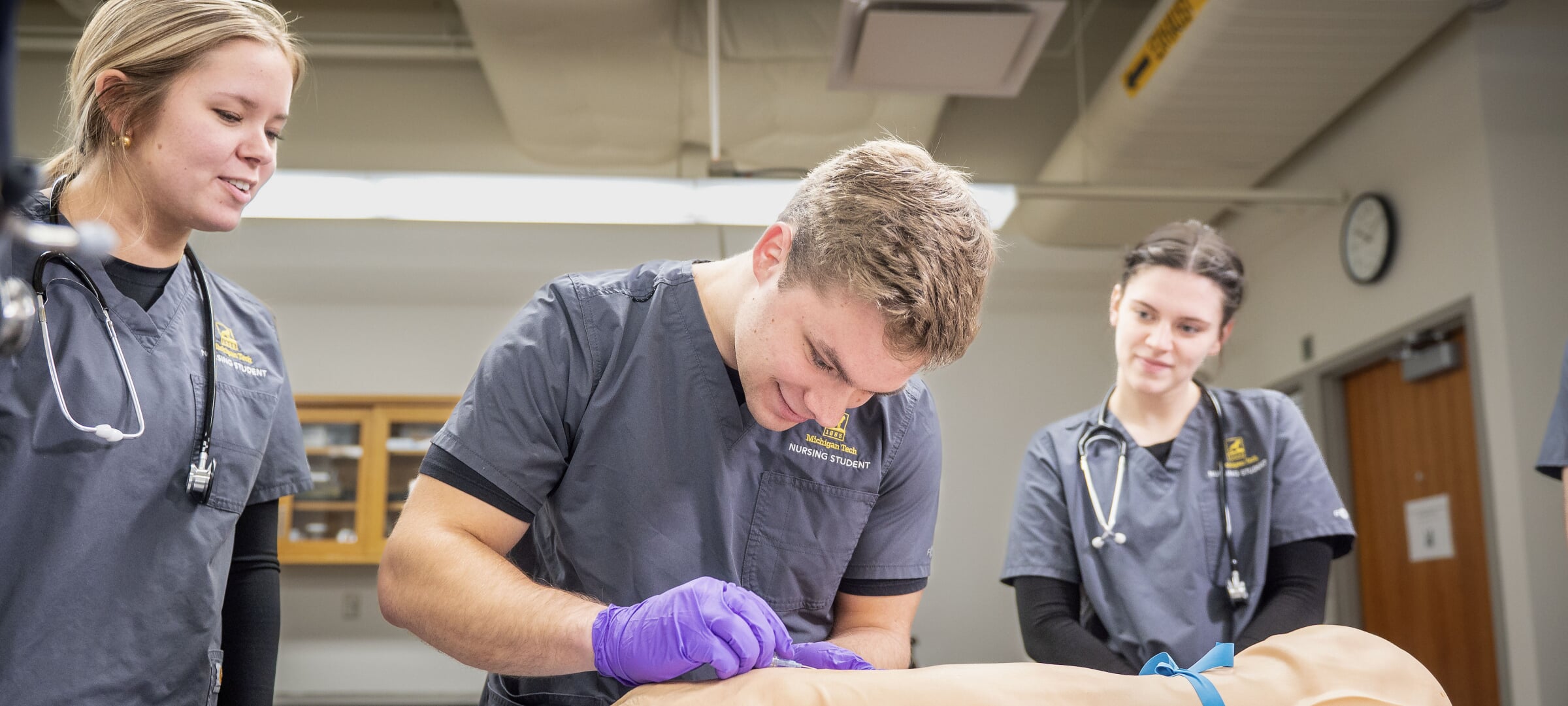 Two students practice nursing techniques under the helpful eye of an instructor
