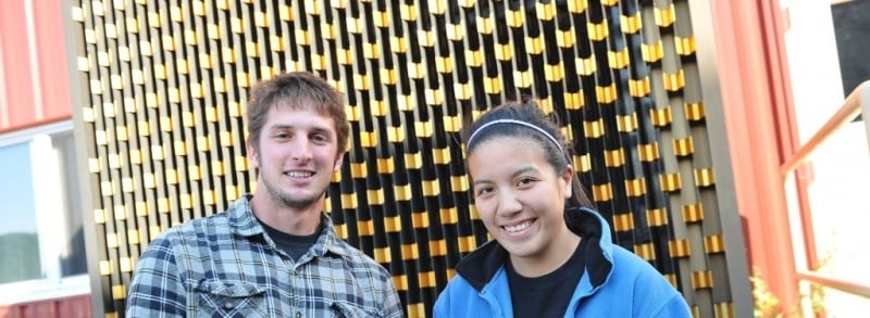 Male and female student standing in front of a colorful wall.