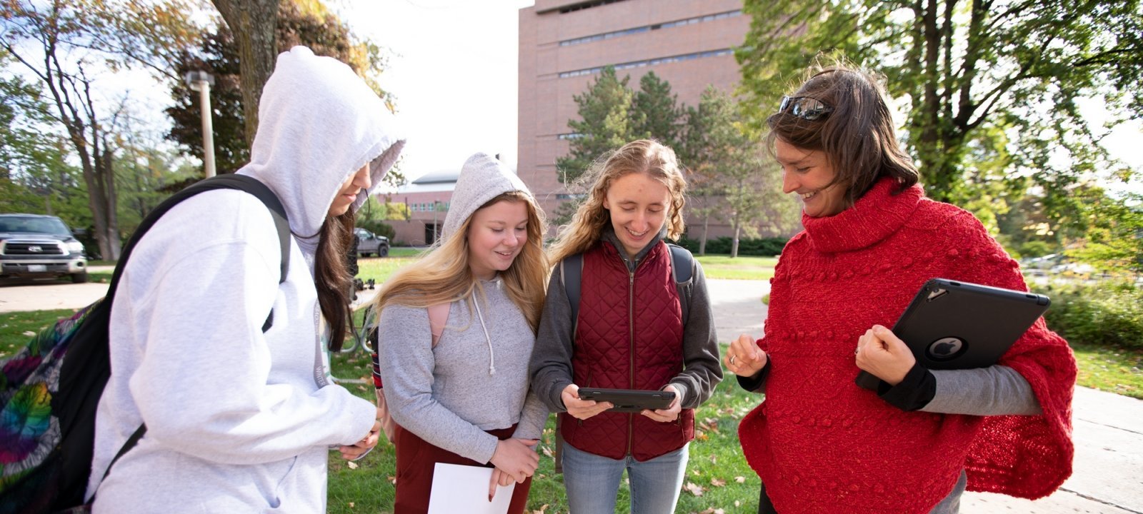 Students and professor having a conversation. One student is holding a tablet while the professor points out information on it.