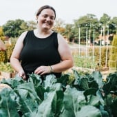 Student standing in front of a raised garden bed of lettuce.