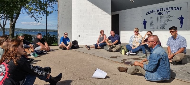 Image of students, many sitting cross-legged on the ground, discussing social issues in a local park