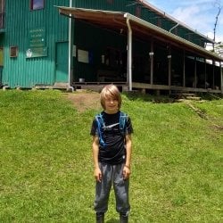 Child wearing a backpack poses for a picture in front of a green building.