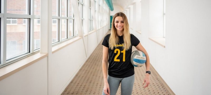 Lauren Fallu standing in a hallway holding a volleyball.
