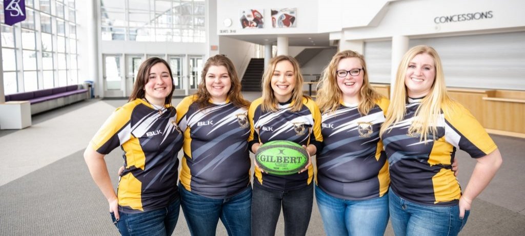 Five women in rugby shirts pose for a group photo.