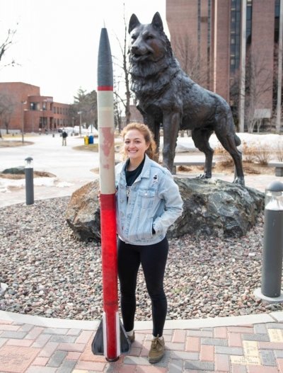 Emi Colman standing in front of the Husky Statue with a rocket.