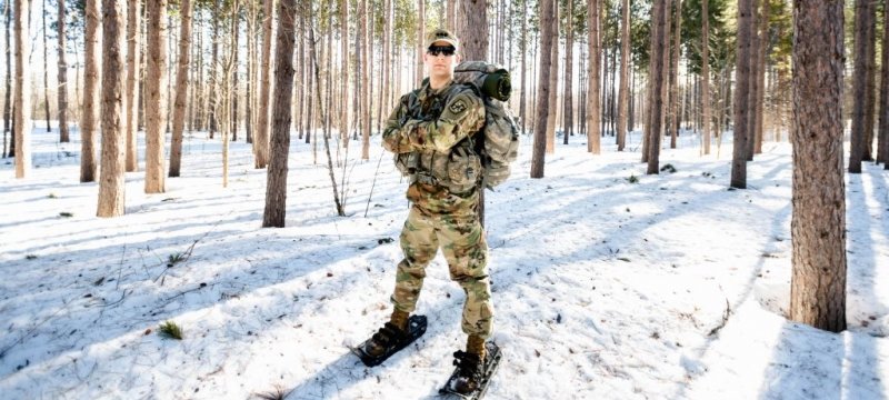 Lucas Grulke, wearing army fatigues, on snowshoes in the woods.