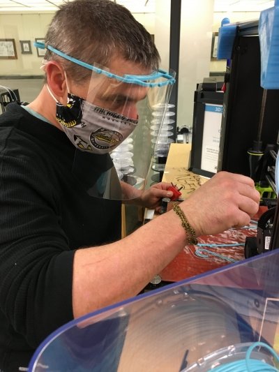 John Schneiderhan wearing a face shield and using a 3-D printer.