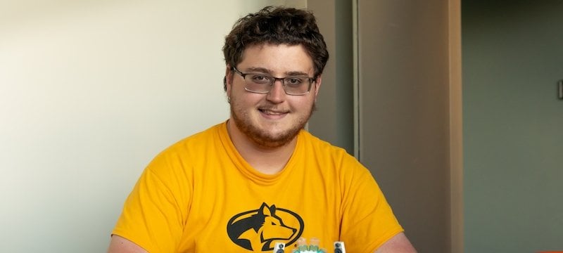 A young man wearing a Michigan Tech t-shirt sits with LEGO products at a table.