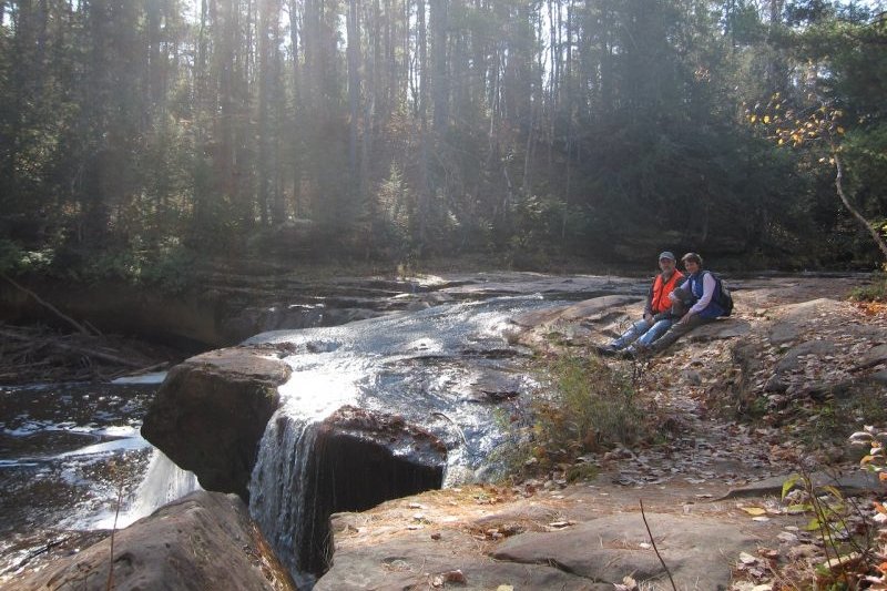 Larry and his wife sitting on rocks next to a waterfall.