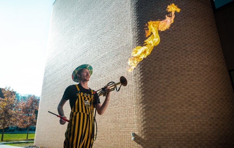 A trumpet player in Huskies Pep Band plays Fight Engineers Fight on his flaming trumpet outside on campus on a sunny fall day.