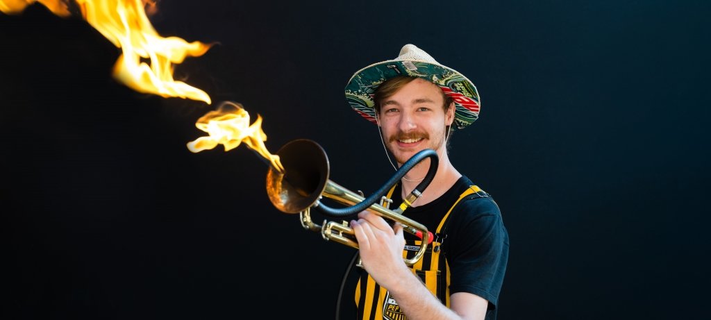 A flaming trumpet player in black and gold striped overalls and a silly hat shows his technique in the Huskies Pep Band.