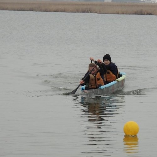 Two college students from Michigan Tech paddle on a lake in their concrete canoe headed for a yellow course marker.