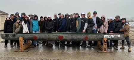 24 members of Michigan Tech Concrete Canoe Team stand behind their canoe Card Shark in a competition at a pond near Wayne State University.