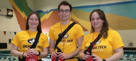 Three lifeguards at the Michigan Tech student development complex pool smile in a photo celebrating their lifesaving award.